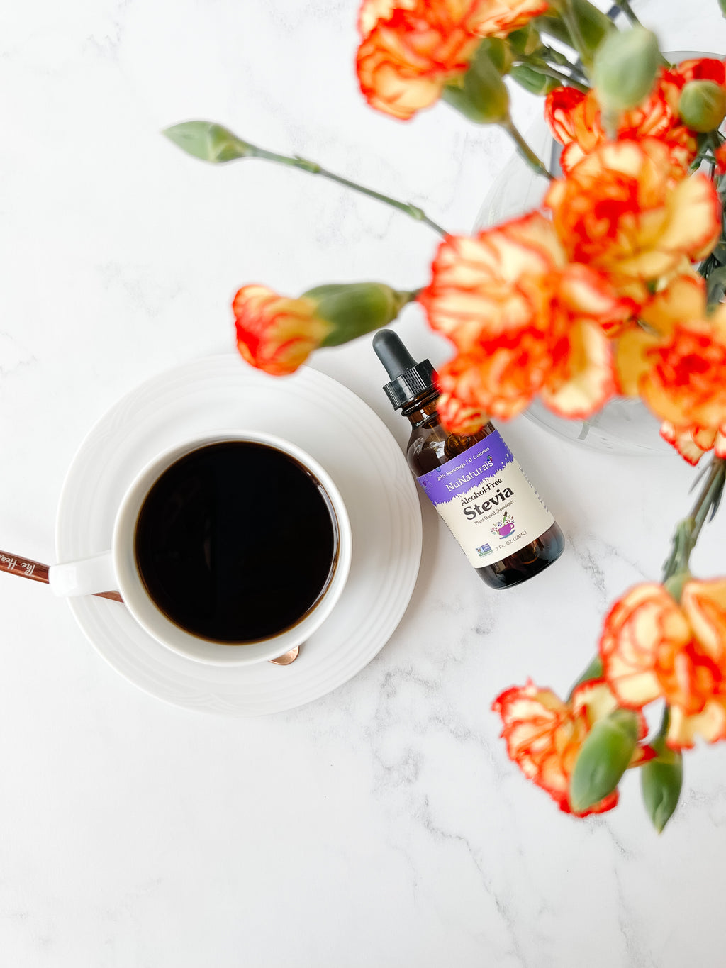 Alcohol-Free Stevia 2 oz dropper bottle on a marble surface beside a cup of black coffee and orange carnations