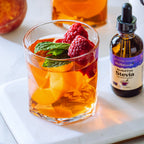 Alcohol-Free Stevia 2 oz dropper bottle beside a glass of peach and raspberry drink with a mint leaf