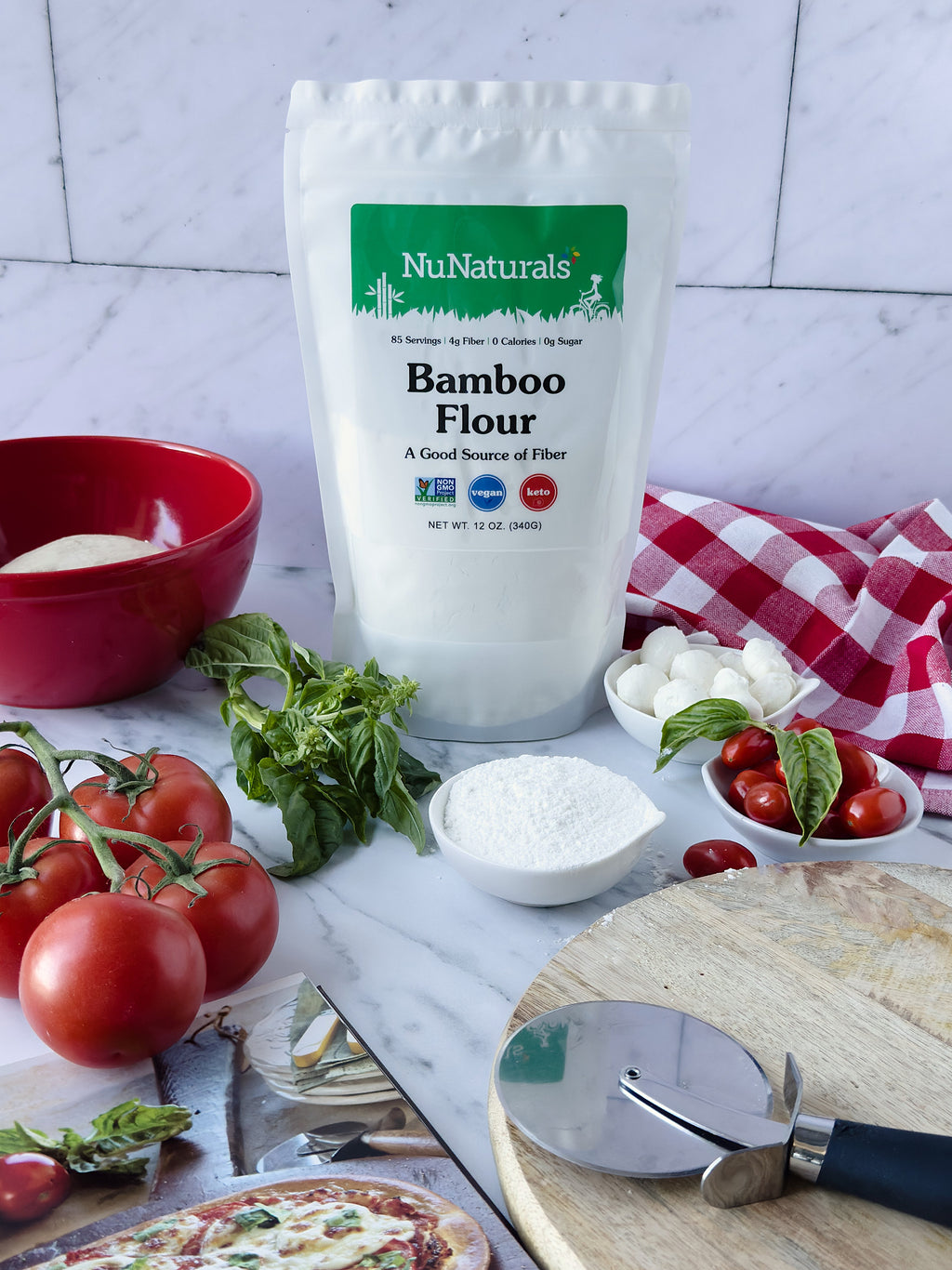 Bamboo Flour pouch on a marble counter with pizza dough, tomatoes, basil, mozzarella balls and a bowl of flour