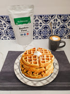 Bamboo Flour bag behind a plate of waffles with cream, next to a mug of latte on a patterned tile counter