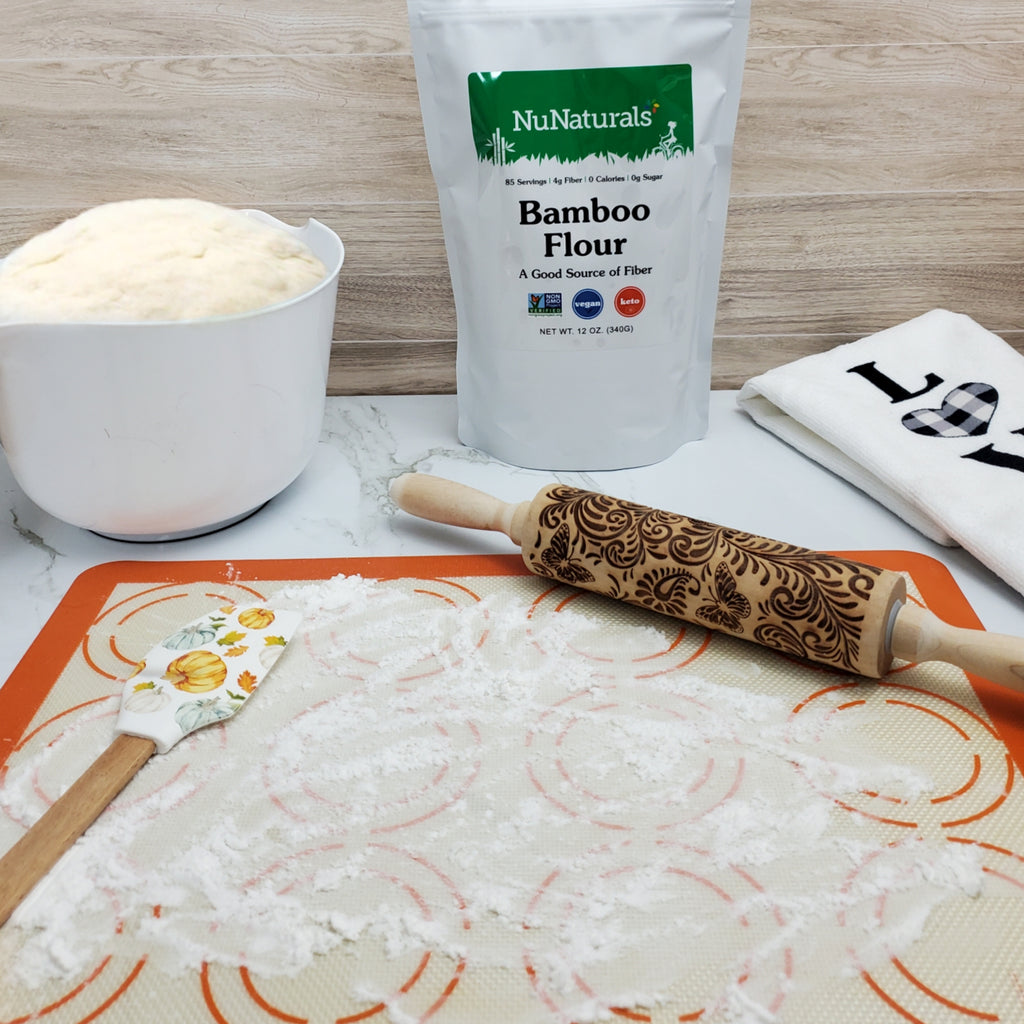 Bamboo Flour pouch behind a bowl of dough, a rolling pin and a spatula on a floured silicone mat