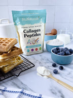 Collagen Peptides pouch behind a stack of waffles, a bowl of blueberries, flour, eggs, and a jug of milk