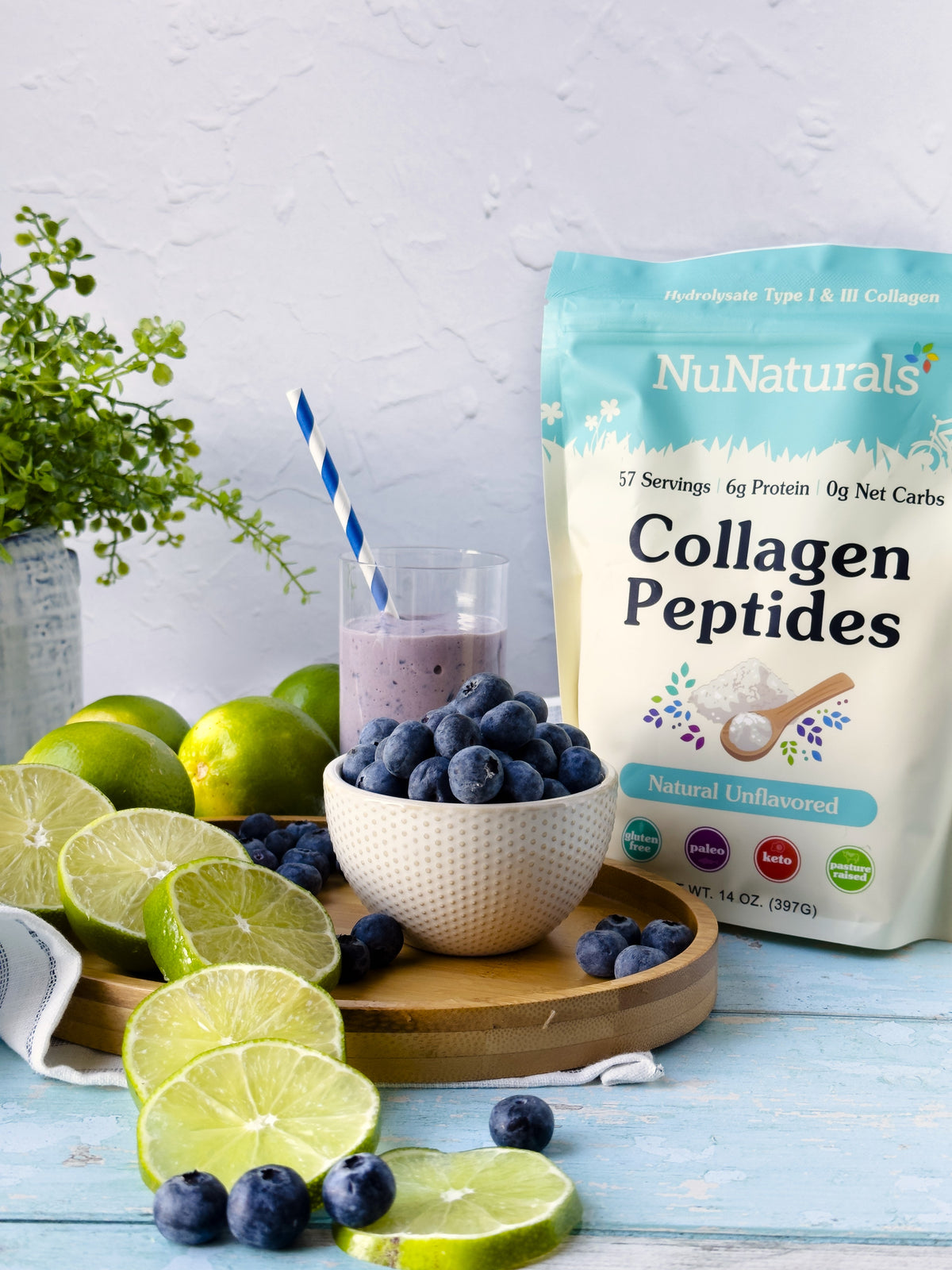 Collagen Peptides pouch beside a bowl of blueberries and a smoothie glass with a striped straw, with limes