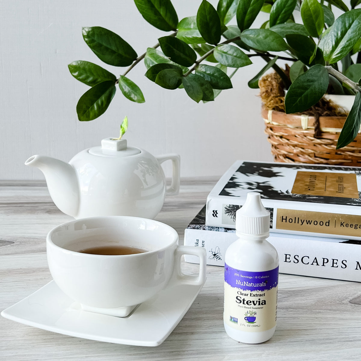 Clear Extract Stevia 2 oz dropper bottle beside a cup of tea and a white teapot, with books and a plant behind