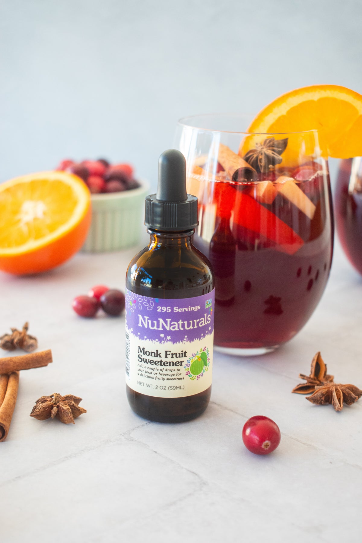 Monk Fruit Sweetener 2 oz dropper bottle in front of a glass of red drink with orange slices, cranberries and cinnamon