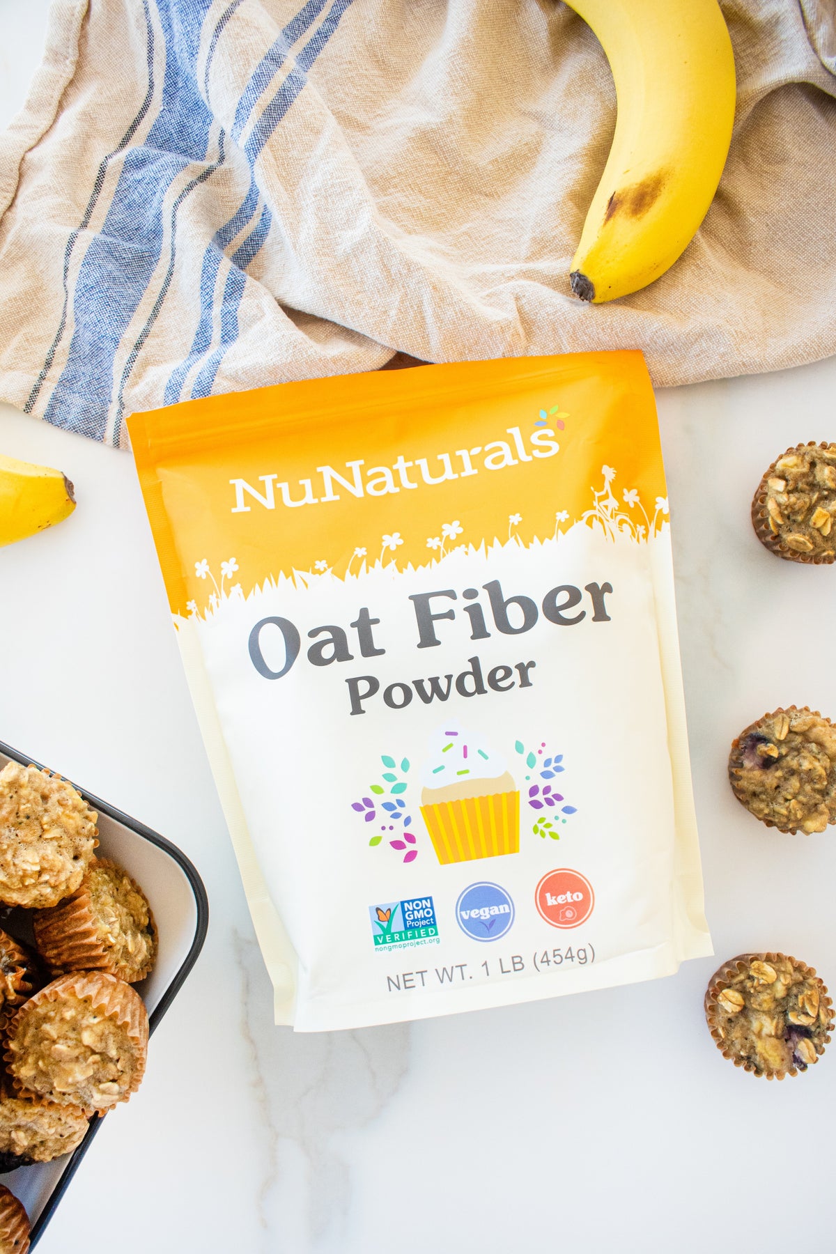 Oat Fiber Powder pouch lying on a marble surface with bananas and oat muffins around it