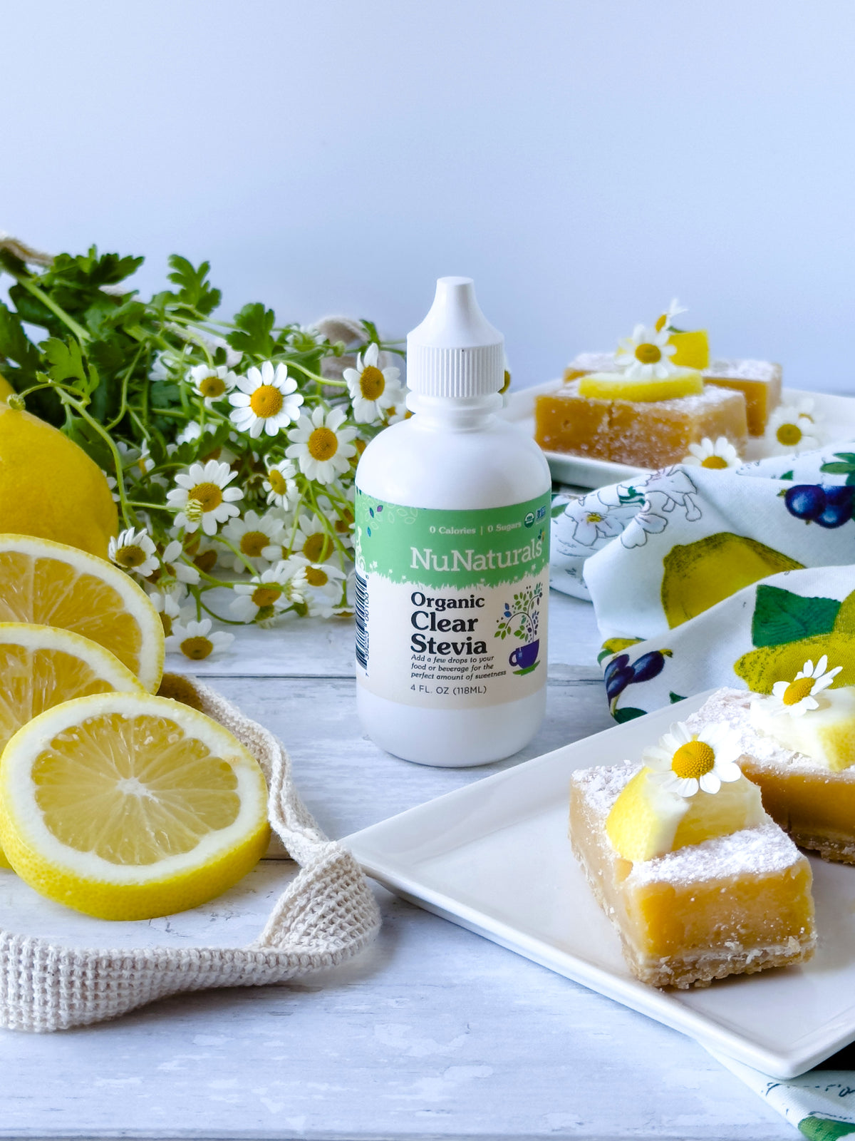 Organic Clear Extract Stevia 4 oz dropper bottle with lemon bars, lemon halves and daisies on a white table