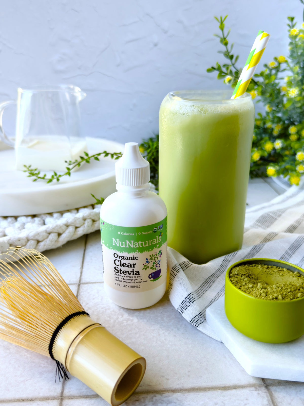 Organic Clear Extract Stevia 4 oz dropper bottle beside a glass of green matcha drink, a whisk and a tin of matcha powder