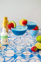 Organic Clear Extract Stevia 4 oz bottle beside a blue cocktail in a coupe glass garnished with strawberry and lime