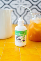 Organic Clear Extract Stevia 4 oz dropper bottle on yellow tile beside a pitcher of iced tea