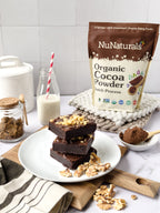 Organic Dutch Cocoa pouch behind a stack of brownies topped with walnuts, with a bottle of milk and a bowl of cocoa powder