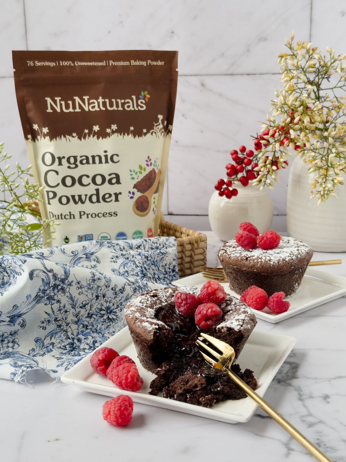 Organic Dutch Cocoa pouch behind chocolate lava cakes topped with raspberries on white plates