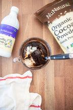 Organic Dutch Cocoa pouch and a vanilla syrup bottle at the frame edges, around a mug cake with ice cream and a spoon