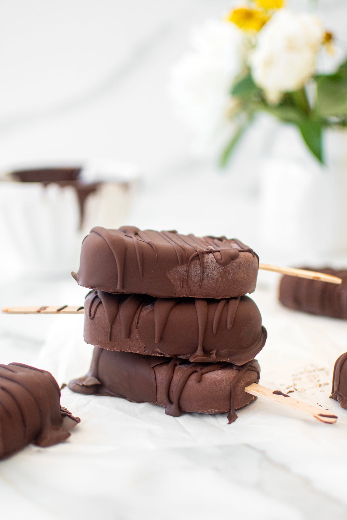 Stack of chocolate-coated frozen bars on wooden sticks, laid on white parchment
