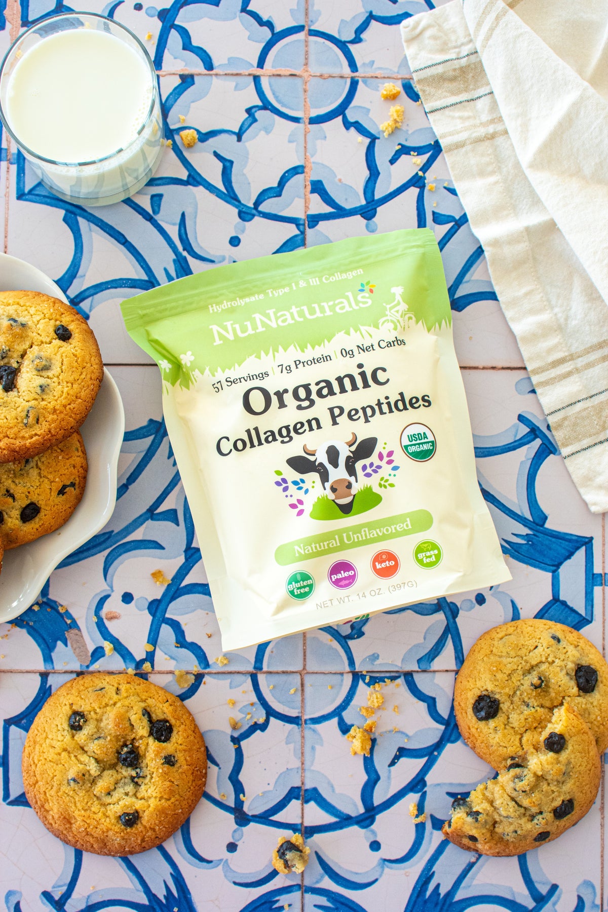 Organic Collagen pouch on patterned tile among chocolate chip cookies, with a plate and a cloth at the edges