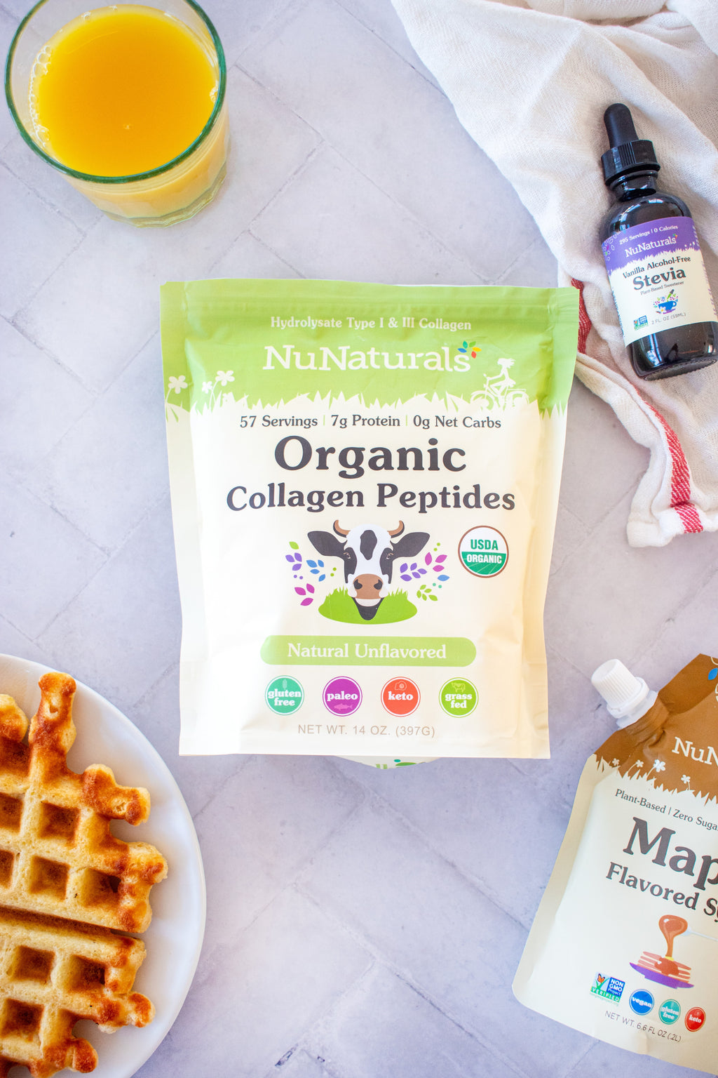 Organic Collagen pouch on a tile counter with a waffle, a vanilla stevia bottle and a syrup pouch at the edges