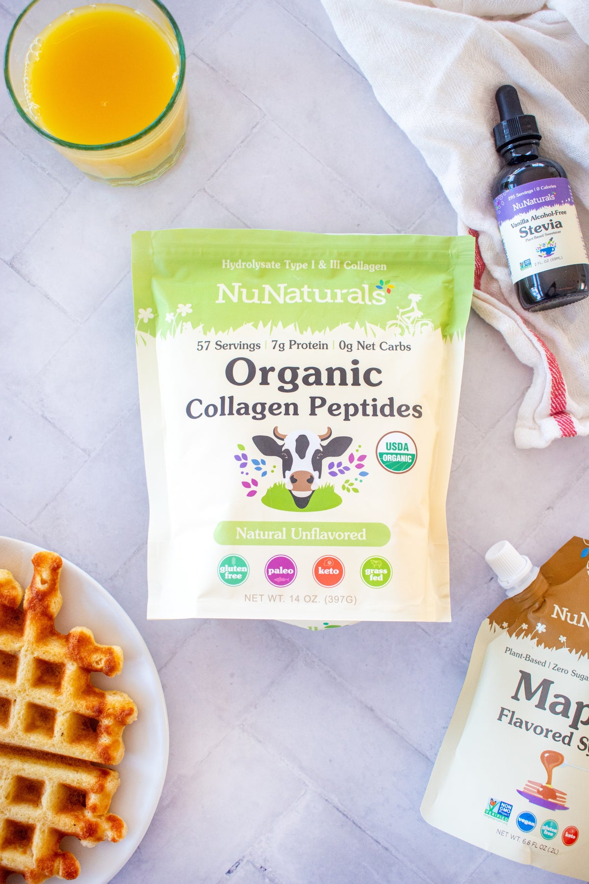 Organic Collagen pouch on a tile counter with a waffle, a vanilla stevia bottle and a syrup pouch at the edges