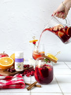 Pure Monk Fruit Sweetener .71 oz shaker beside a pitcher of red sangria pouring into glasses, with cranberries and oranges