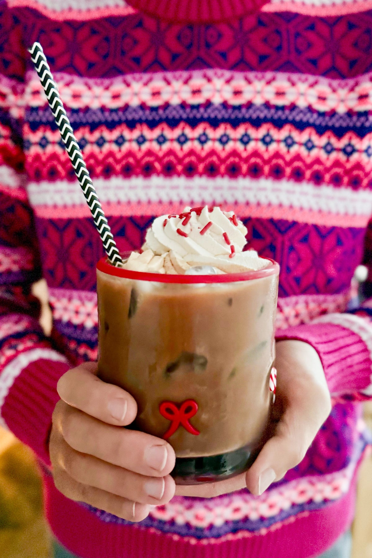 Iced mug drink with whipped cream and a striped straw, held over a knit sweater