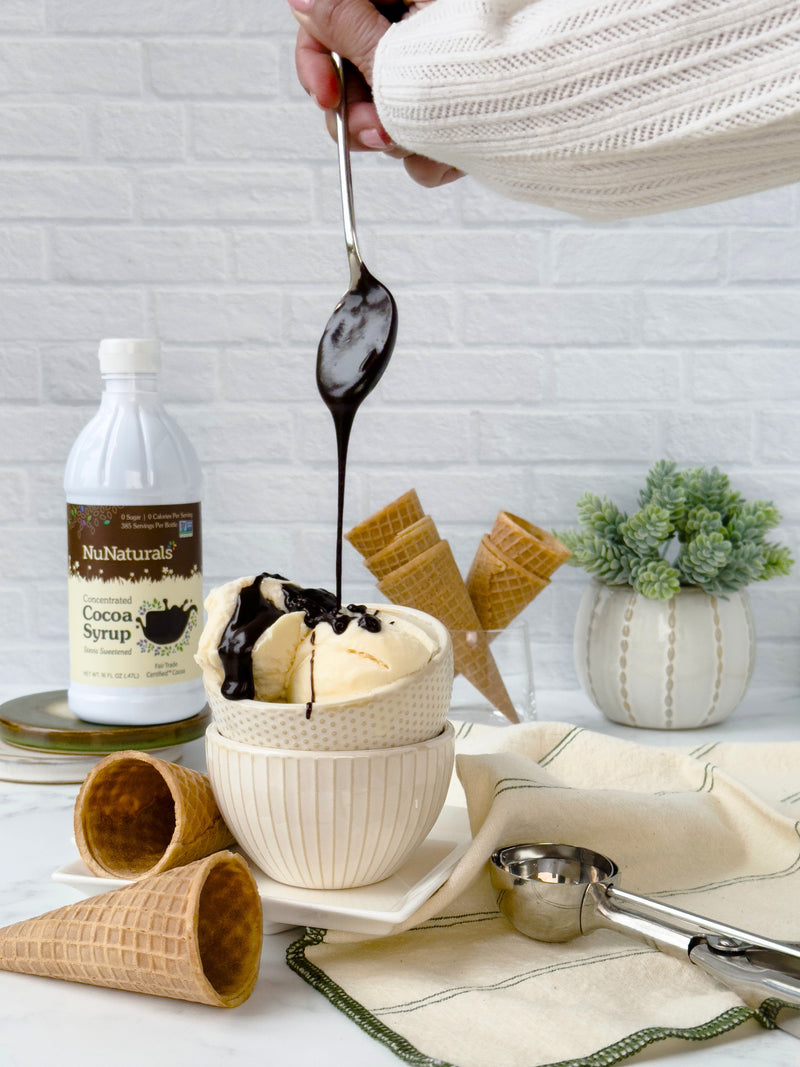 Cocoa Syrup 16 oz bottle beside a bowl of ice cream with syrup drizzled from a spoon, waffle cones behind