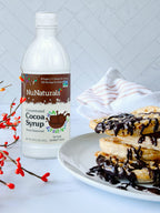 Cocoa Syrup 16 oz bottle beside a plate of pastries drizzled with chocolate, with red berry branches in front