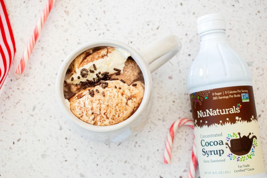 Cocoa Syrup 16 oz bottle at the edge of the frame beside a mug of dessert topped with chocolate sprinkles and a candy cane