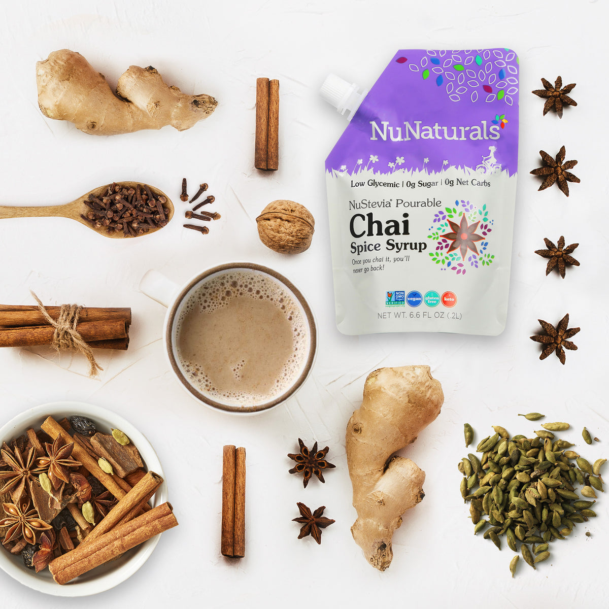 Chai Spice Syrup 6.6 oz pouch surrounded by ginger, cinnamon sticks, star anise, cloves and cardamom, next to a mug of chai