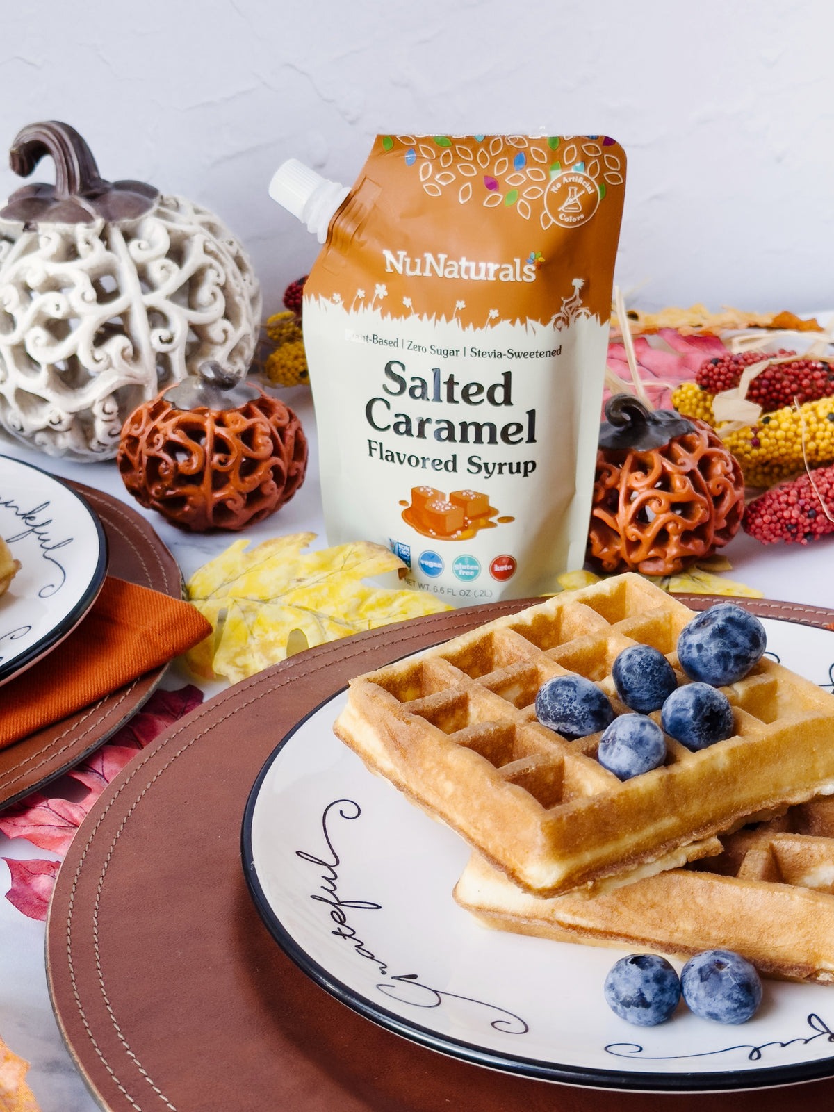 Salted Caramel Flavored Syrup 6.6 oz pouch behind a plate of waffles topped with blueberries, with autumn decor