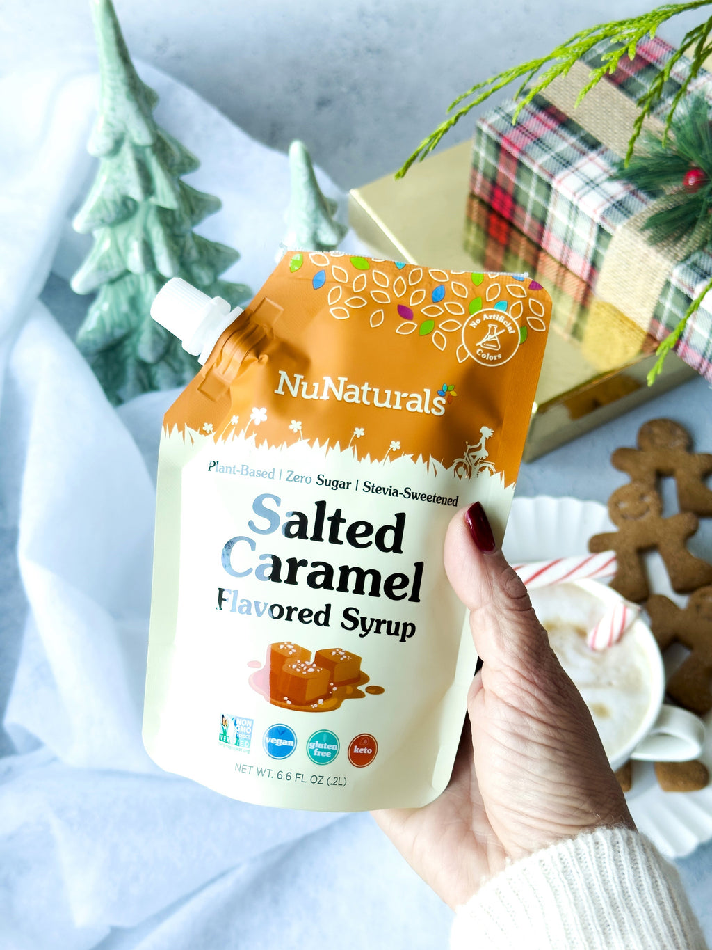 Salted Caramel Flavored Syrup 6.6 oz pouch held in one hand with gingerbread cookies and gift boxes nearby