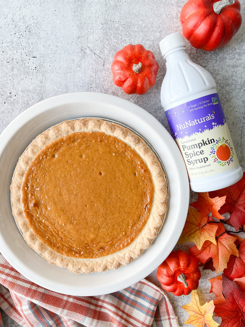 Pumpkin Spice Syrup 16 oz bottle beside a whole pumpkin pie in a white dish, with small pumpkins and autumn leaves