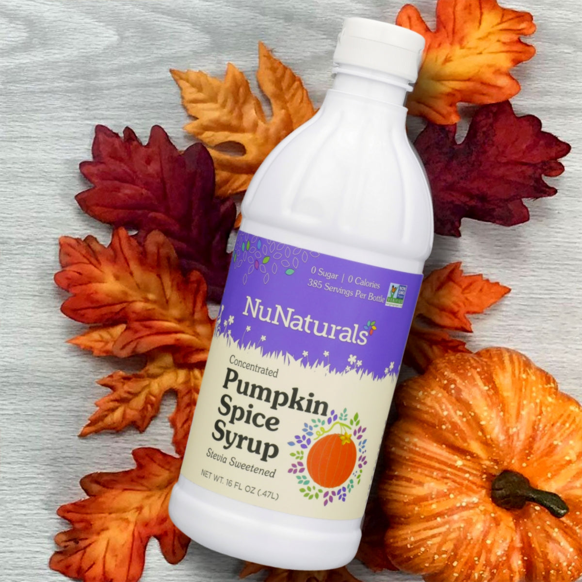 Pumpkin Spice Syrup 16 oz bottle lying on autumn leaves next to an orange pumpkin
