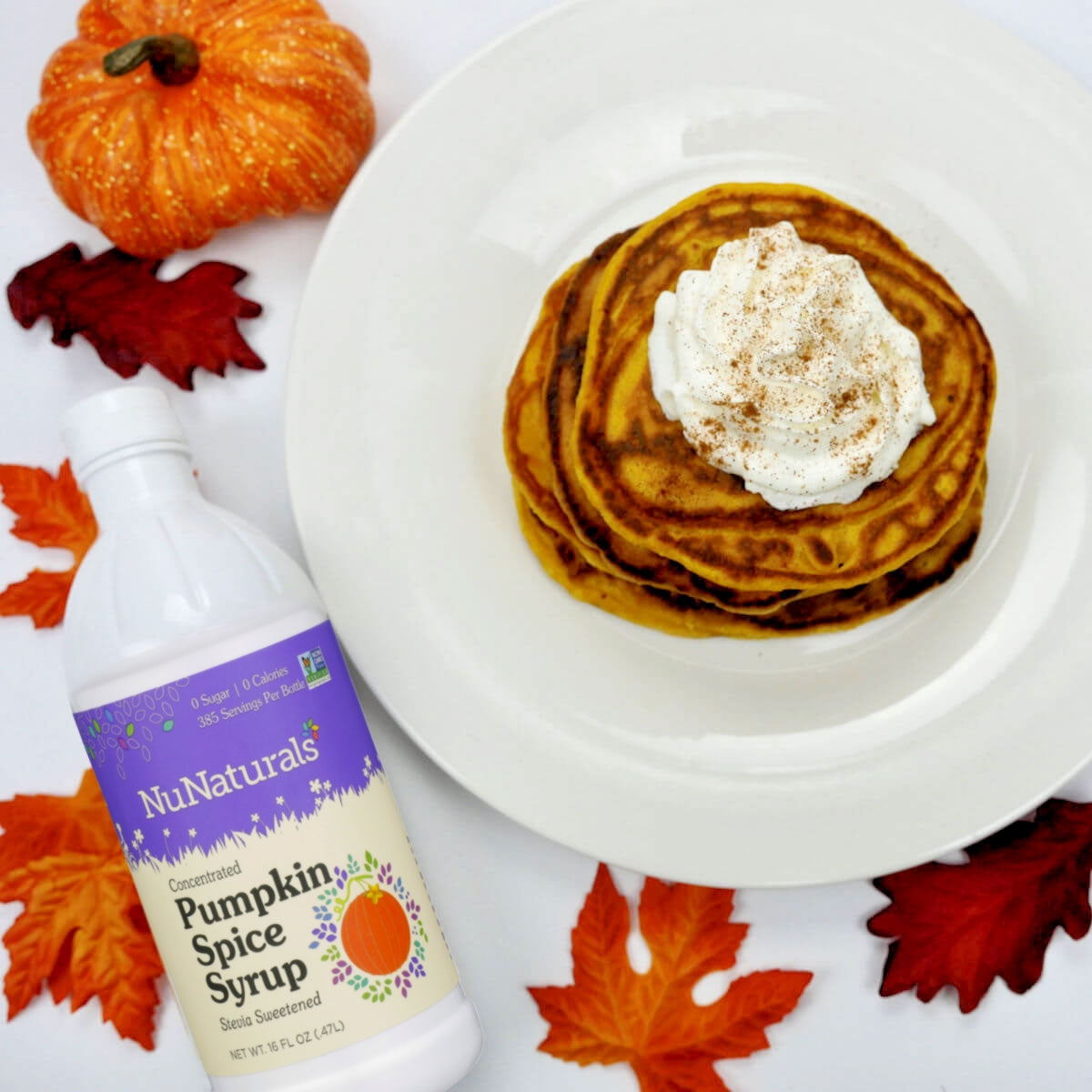 Pumpkin Spice Syrup 16 oz bottle beside a plate of pancakes with whipped cream, pumpkins and autumn leaves