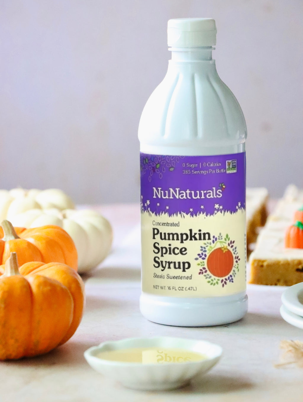 Pumpkin Spice Syrup 16 oz bottle standing among orange and white pumpkins, with bars on plates behind it
