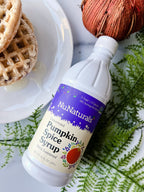 Pumpkin Spice Syrup 16 oz bottle lying on green fern leaves next to waffles on a white plate