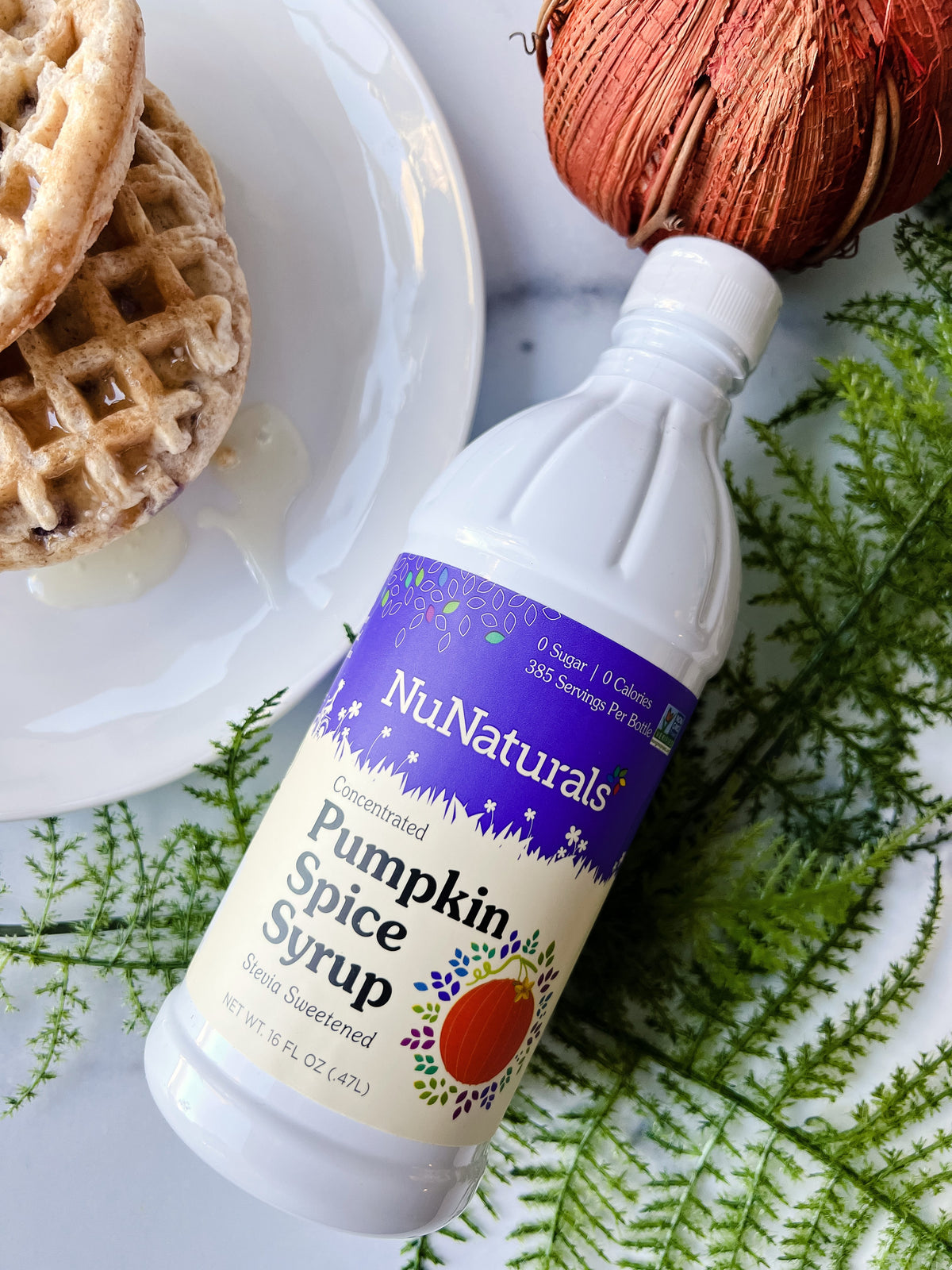 Pumpkin Spice Syrup 16 oz bottle lying on green fern leaves next to waffles on a white plate