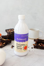 Pumpkin Spice Syrup 16 oz bottle standing among brownies topped with pecans, with a white mug behind