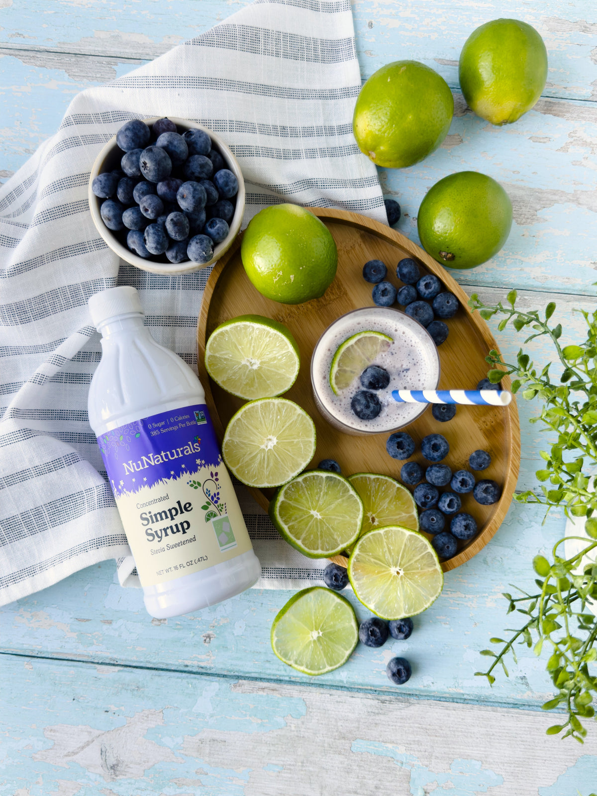 Simple Syrup 16 oz bottle on a blue wooden table with limes, blueberries and a blueberry drink in a glass