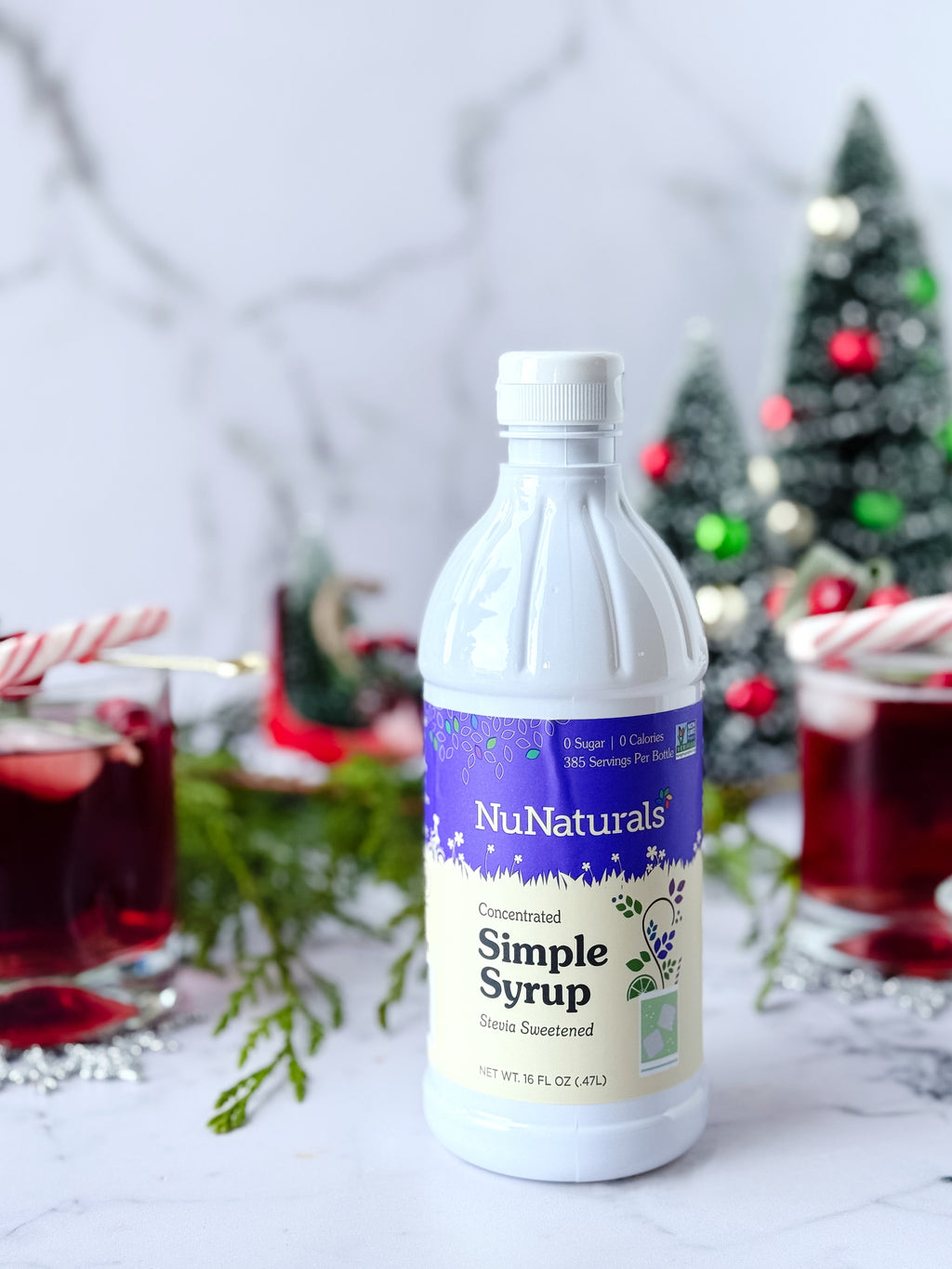 Simple Syrup 16 oz bottle on a marble counter with two red drinks, candy canes and small holiday trees behind