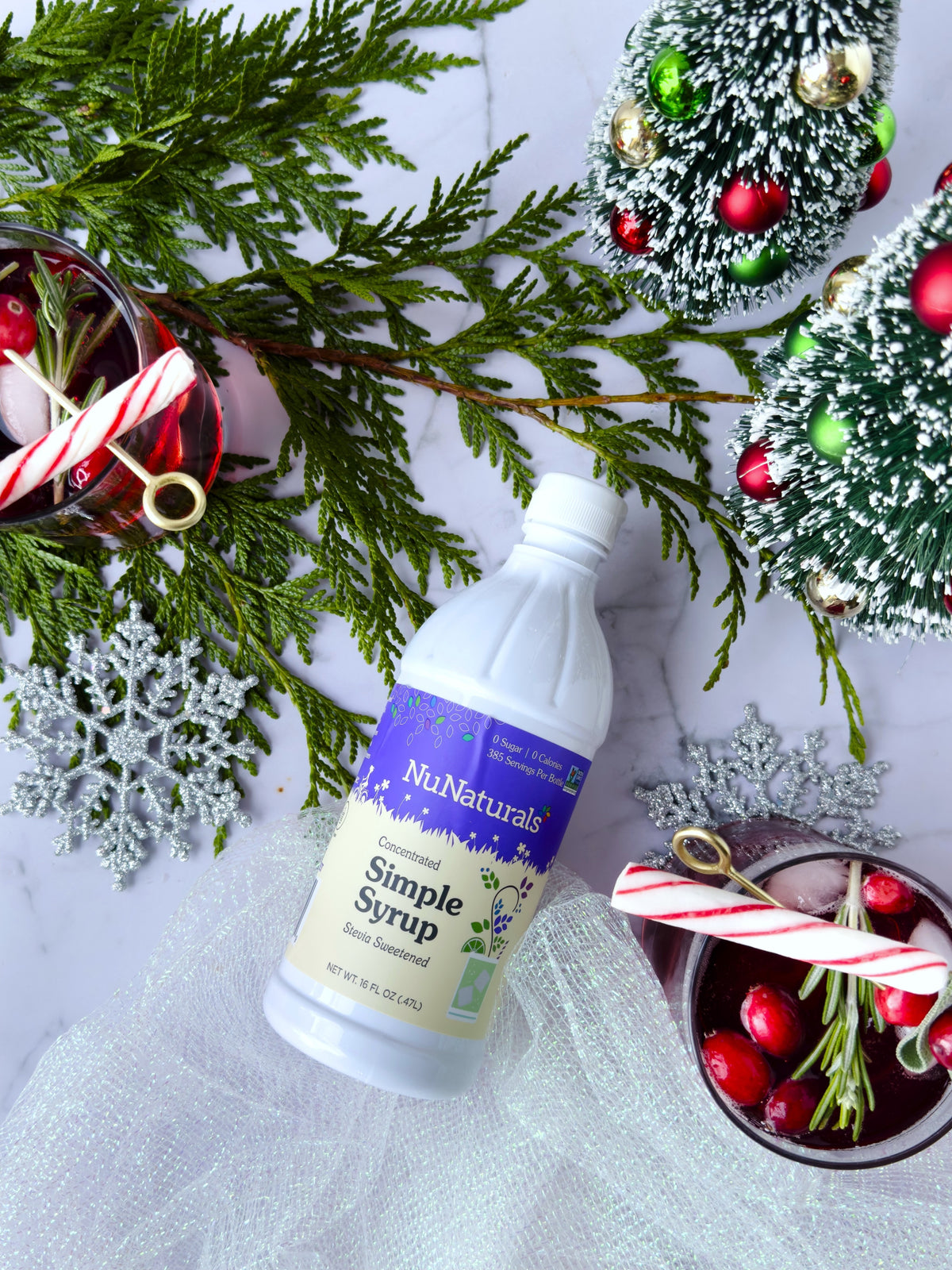 Simple Syrup 16 oz bottle lying on a table with evergreen sprigs, ornaments, cranberries, and candy cane stirrers