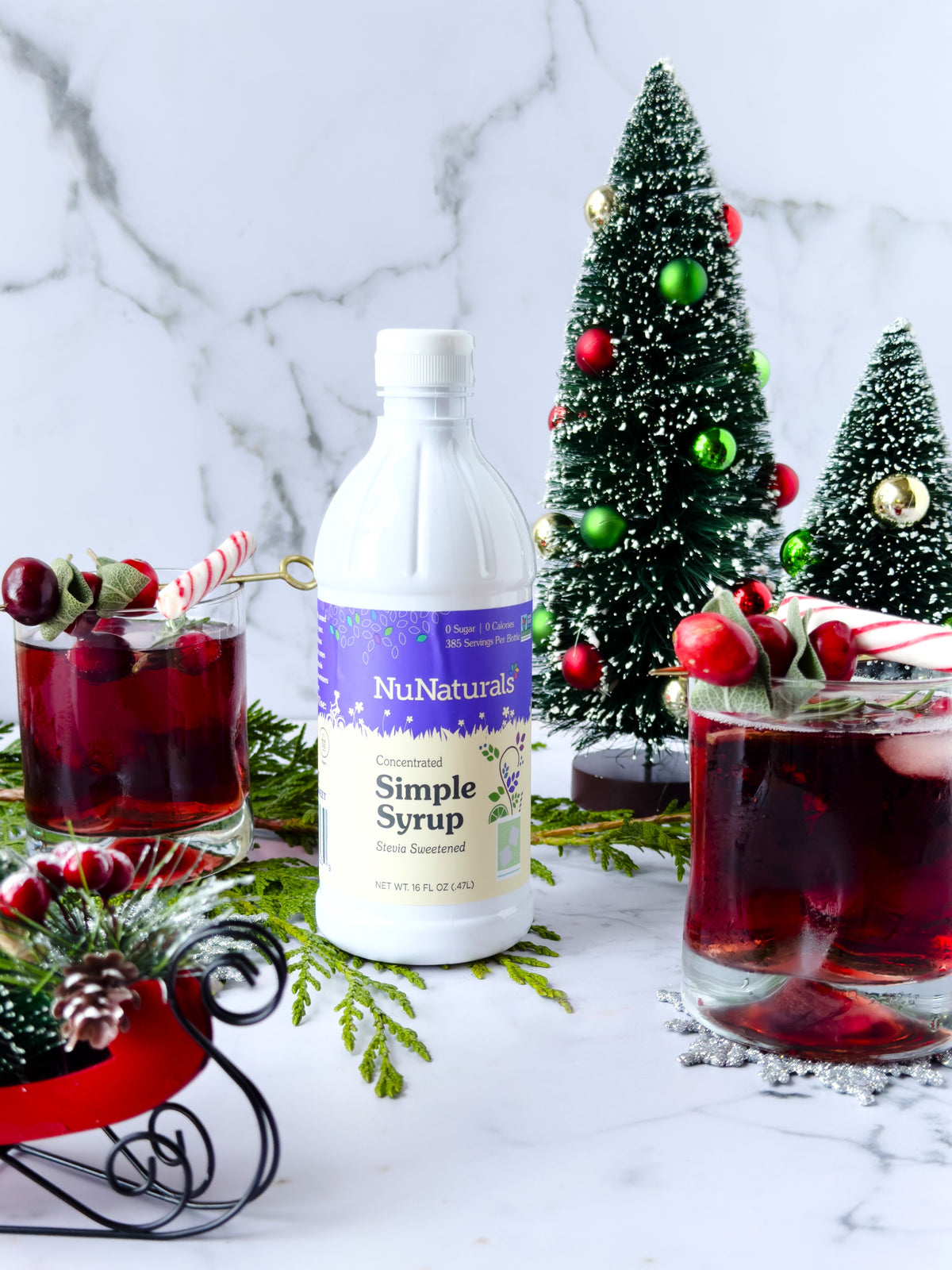 Simple Syrup 16 oz bottle in front of two red drinks with candy cane stirrers and small holiday trees