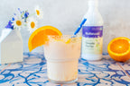 Simple Syrup 16 oz bottle behind a ribbed glass of creamy drink with an orange slice and blue straw, on patterned tile