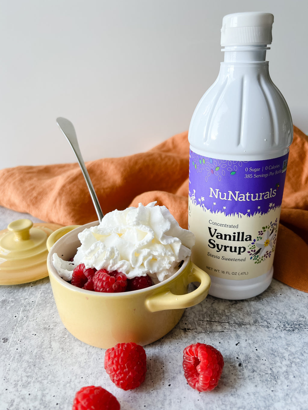 Vanilla Syrup 16 oz bottle behind a small yellow dish of whipped cream and raspberries
