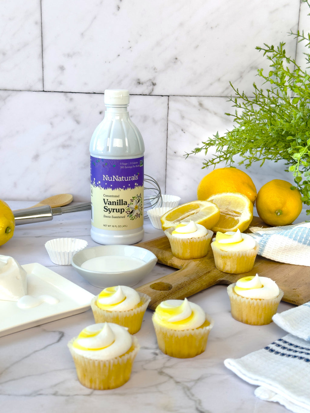 Vanilla Syrup 16 oz bottle on a marble counter with lemon cupcakes, lemons and a small bowl of liquid