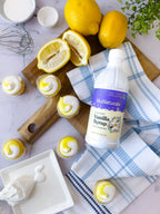 Vanilla Syrup 16 oz bottle lying on a blue checked towel beside lemons and lemon cupcakes with white frosting