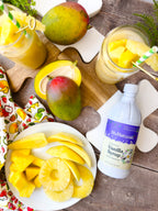 Vanilla Syrup 16 oz bottle on a wooden board beside sliced mango, pineapple rings, and glasses of fruit drink