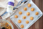 Simple Syrup bottle at the corner of a baking sheet lined with rows of oat cookie dough balls, with a striped towel