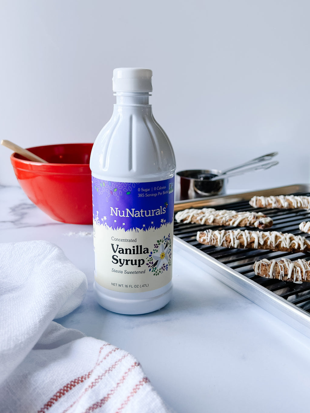 Vanilla Syrup 16 oz bottle on a counter beside a red mixing bowl and a tray of iced cookies