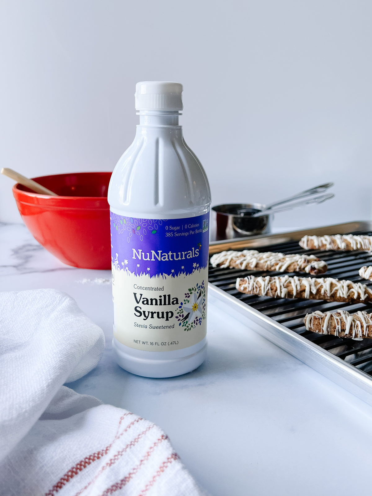 Vanilla Syrup 16 oz bottle on a counter beside a red mixing bowl and a tray of iced cookies