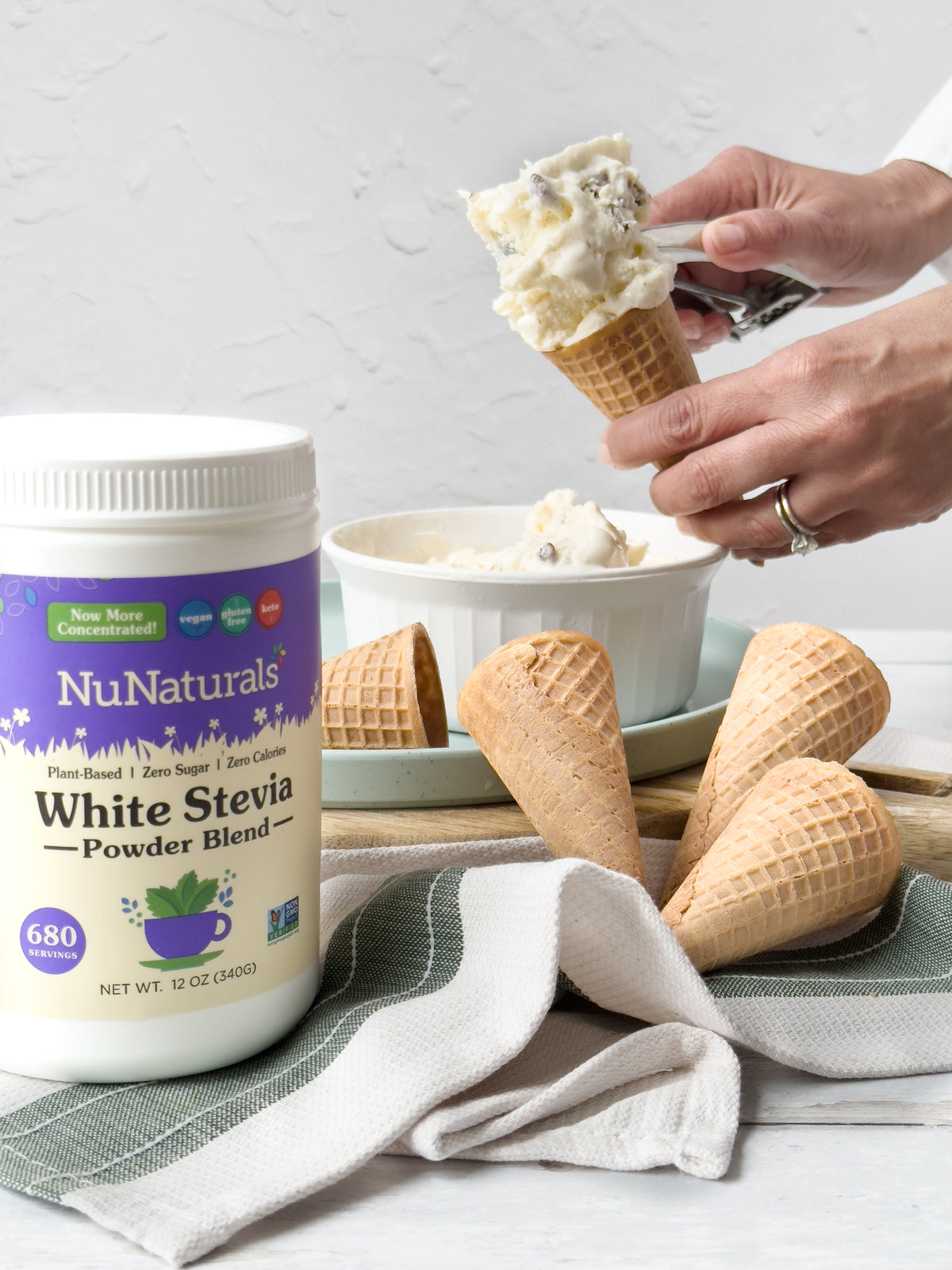 White Stevia Powder jar in front of hands scooping ice cream into a waffle cone, with more cones on a towel