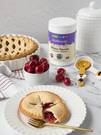 White Stevia Powder jar on a marble counter with cherry pie, a bowl of cherries and a honey dipper spoon